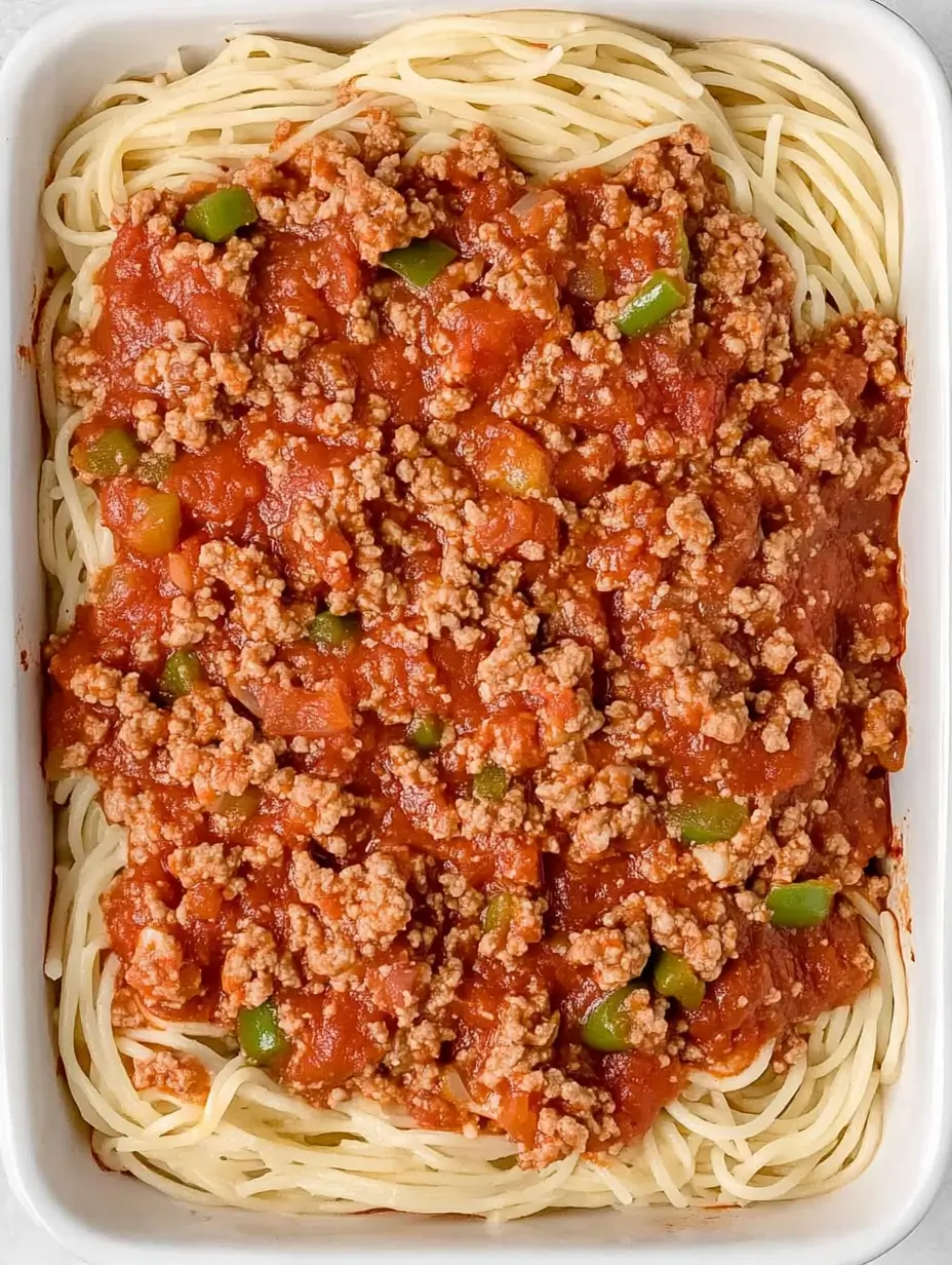 MILLION DOLLAR SPAGHETTI ALFREDO 6 A baking dish with a layer of cooked spaghetti topped with hearty meat sauce, ready for assembly.