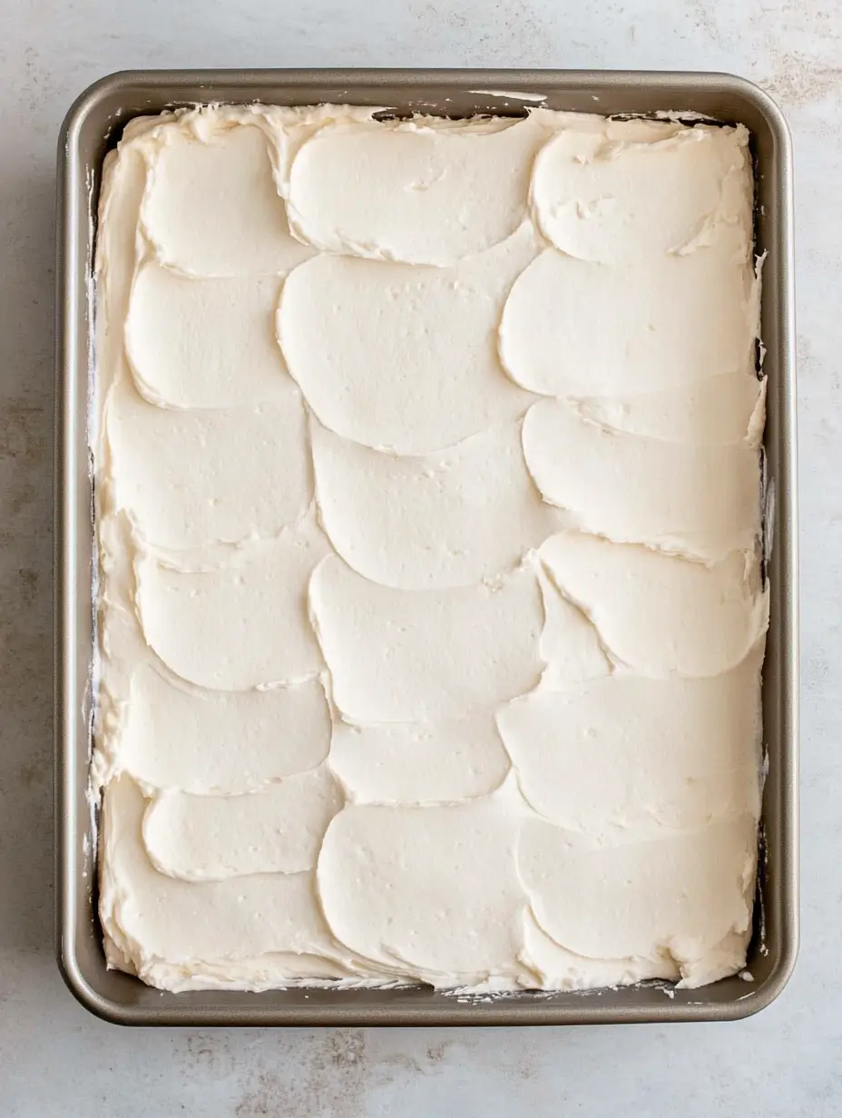 A rectangular pan filled with a smooth layer of white cream cheese frosting, evenly spread.