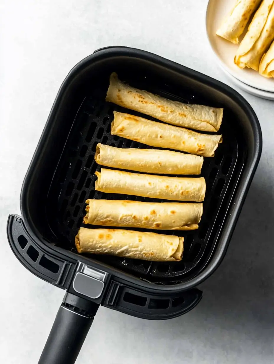 Ridiculously Good Air Fryer Flautas 17 Overhead shot of cooked flautas arranged in an air fryer basket, showing their golden-brown, crispy texture.