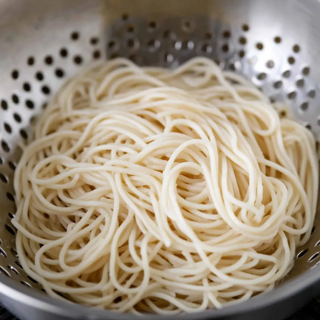 A metal colander filled with freshly cooked and drained noodles.