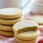 Matcha Shortbread Cookies 12 matcha-shortbread-cookies-stacked-with-one-cookie-bitten-showing-green-interior-on-pink-cloth