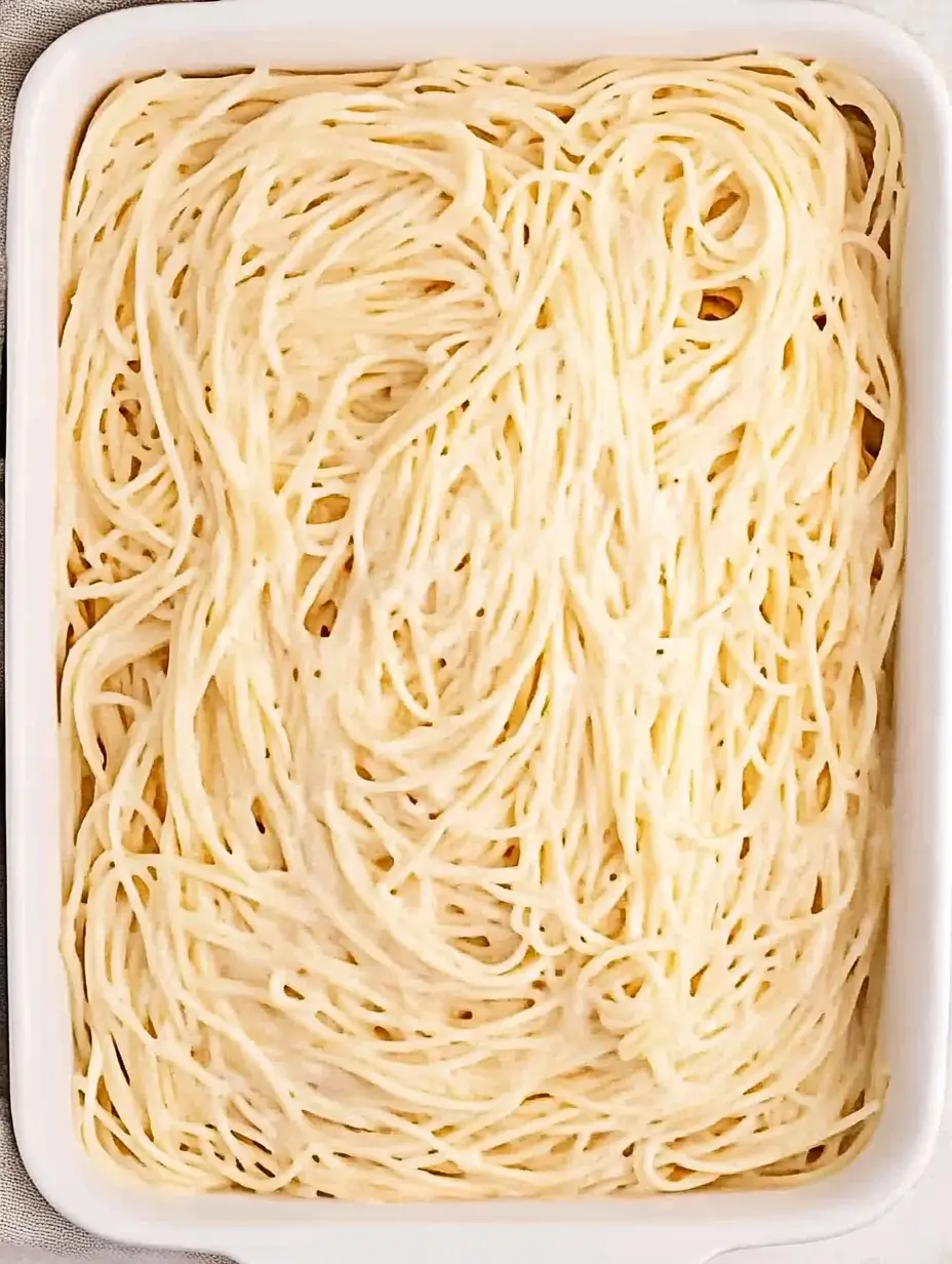 MILLION DOLLAR SPAGHETTI ALFREDO 5 A baking dish filled with cooked spaghetti coated in creamy Alfredo sauce, ready for layering.