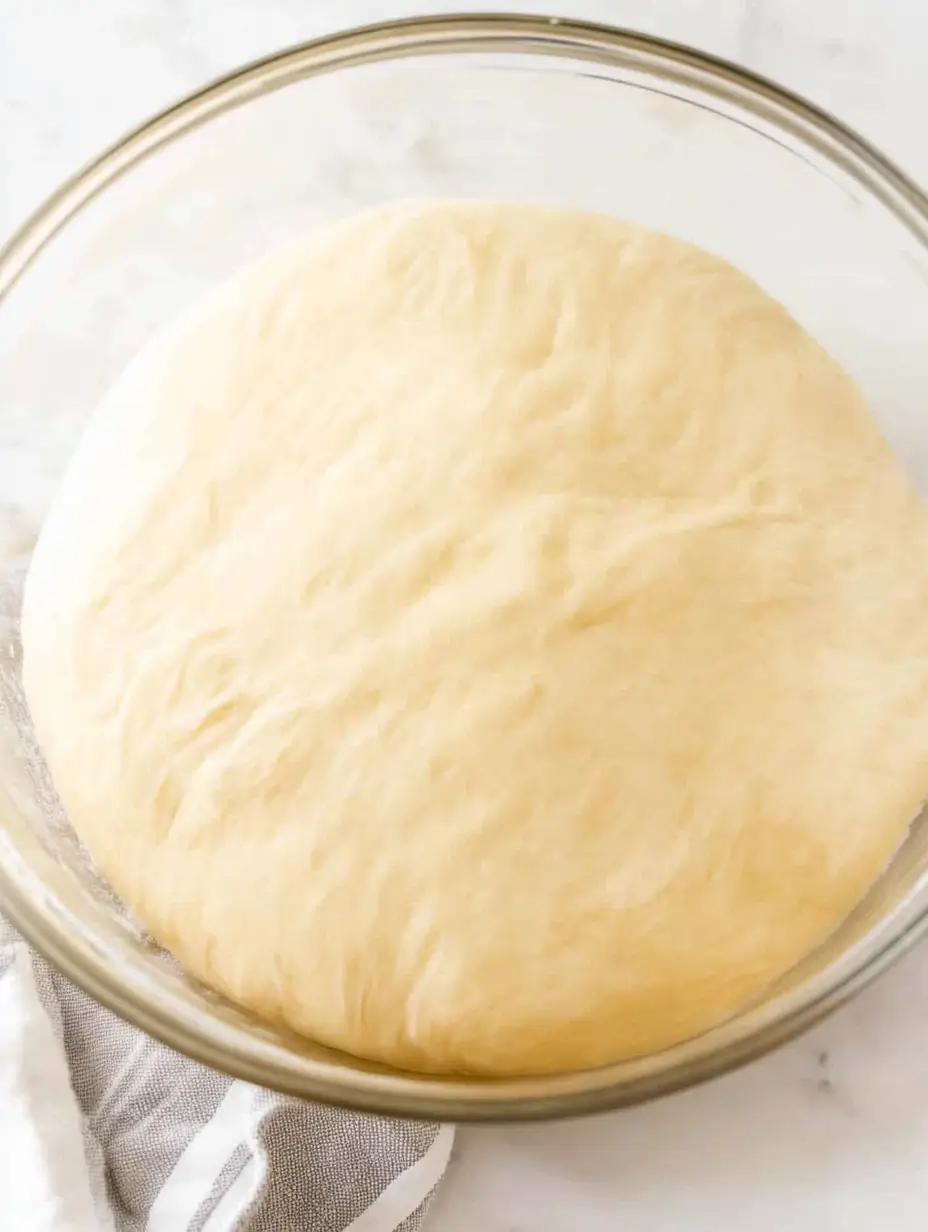 Pecan Rolls 4 proofed-dough-in-a-glass-bowl-smooth-pale-yellow-dough-ready-for-baking-gray-striped-towel-underneath