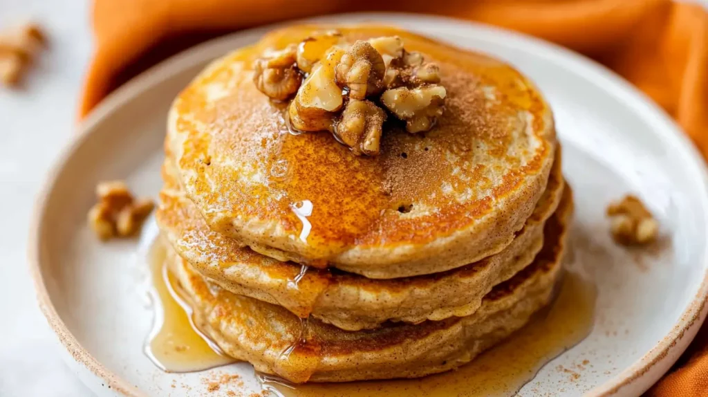 Close-up of pumpkin protein pancakes topped with crunchy walnuts and maple syrup glistening on top.