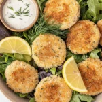 Juicy Air Fryer Chicken Patties 14 Breaded and crispy chicken patties served on a bed of mixed greens with lemon wedges and a creamy dipping sauce garnished with fresh dill.