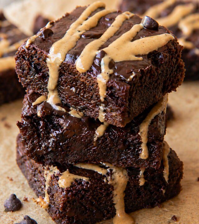 cottage cheese brownies stacked with peanut butter drizzle and chocolate chips on parchment paper
