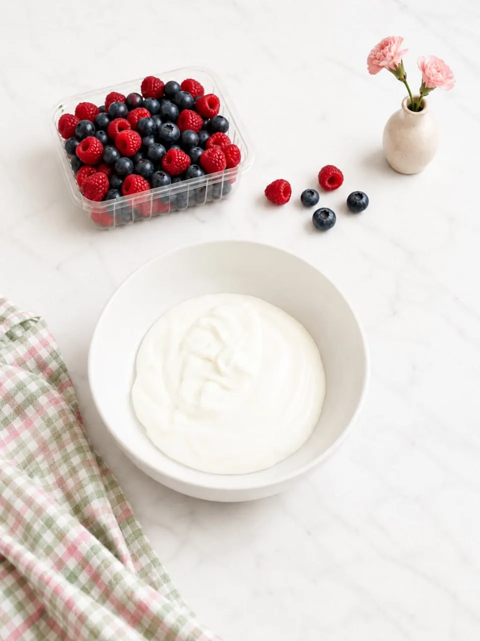 Bowl of thick Greek yogurt beside a container of fresh berries